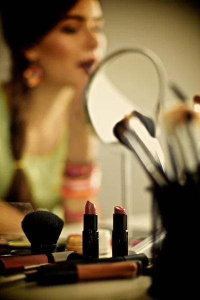 Joven hermosa mujer haciendo maquillaje cerca del espejo, sentado en el escritorio —  Fotos de Stock