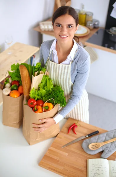 Mujer con bolsas de compras en la cocina en casa, de pie cerca del escritorio — Foto de Stock