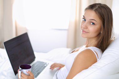 Yatak ve çay tadını çıkarırken bir dizüstü bilgisayar ile genç ve güzel bir kadın