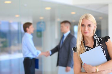 Arka planda tokalaşırken iş adamları ile bir ofiste ayakta bir güzel ofis çalışanı portresi