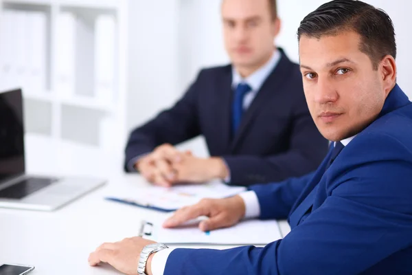 Porträt eines gutaussehenden Geschäftsmannes, der in einem Büro sitzt und im Hintergrund Kollegen hat — Stockfoto