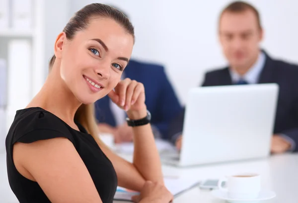 Retrato de una hermosa mujer de negocios sentada en una oficina con colegas en el fondo —  Fotos de Stock