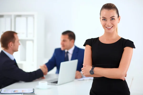 Porträt einer schönen Geschäftsfrau, die in einem Büro steht und Kollegen im Hintergrund die Hände schütteln — Stockfoto