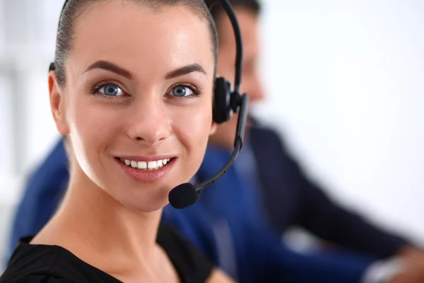 Retrato de mulher de negócios bonita em fones de ouvido sorrindo com colegas de fundo — Fotografia de Stock