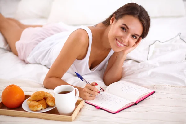 Young beautiful woman lying in bed writing a diary