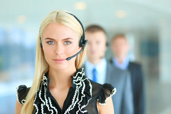 Retrato de mujer de negocios hermosa en auriculares sonriendo con colegas de fondo —  Fotos de Stock