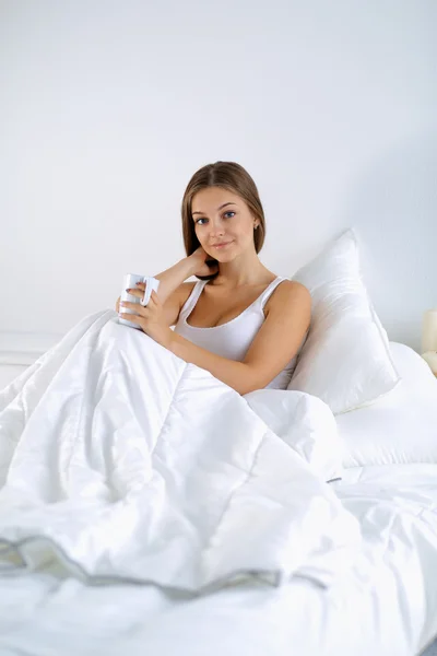 Una hermosa joven en la cama disfrutando de una taza de té — Foto de Stock