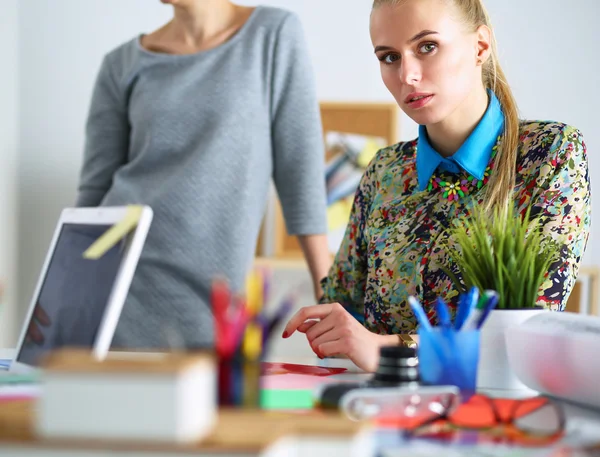 Porträt einer schönen Büroangestellten, die in einem Büro sitzt und einen Kollegen hinter sich hat — Stockfoto