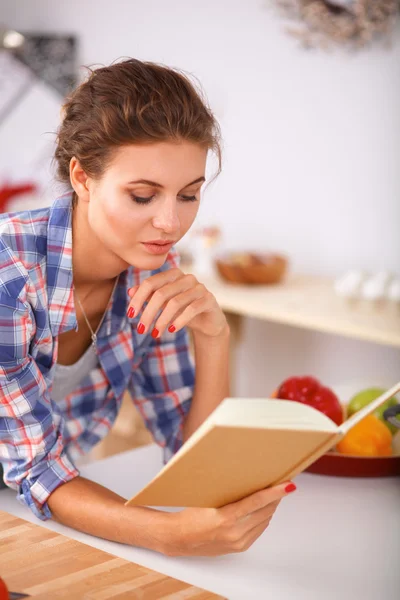 Uma bela jovem mulher lendo um livro de receitas em sua cozinha — Fotografia de Stock