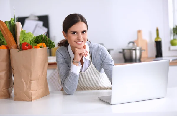 Hermosa joven cocina mirando a la pantalla del ordenador portátil con recibo en la cocina —  Fotos de Stock