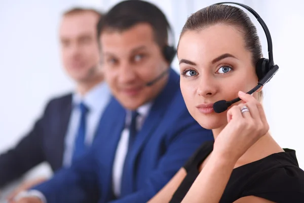 Retrato de mulher de negócios bonita em fones de ouvido sorrindo com colegas de fundo — Fotografia de Stock