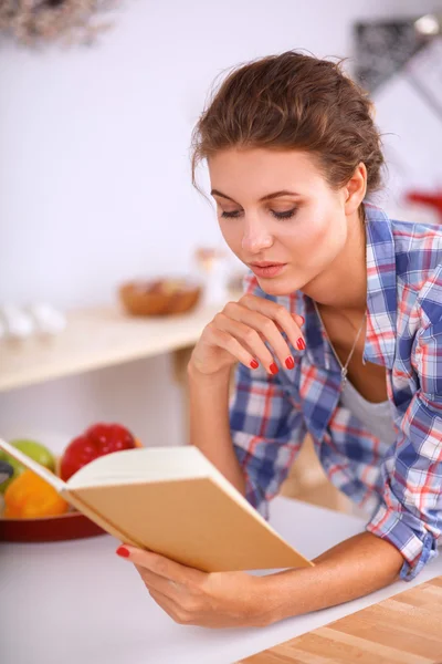 Uma bela jovem mulher lendo um livro de receitas em sua cozinha — Fotografia de Stock