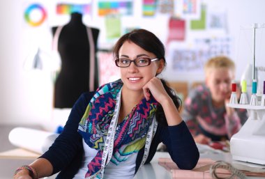 Güzel moda tasarımcısı stüdyoda masada oturuyor.