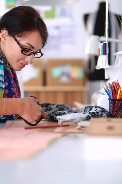Mode-ontwerper snijden textiel naast een naaimachine — Stockfoto