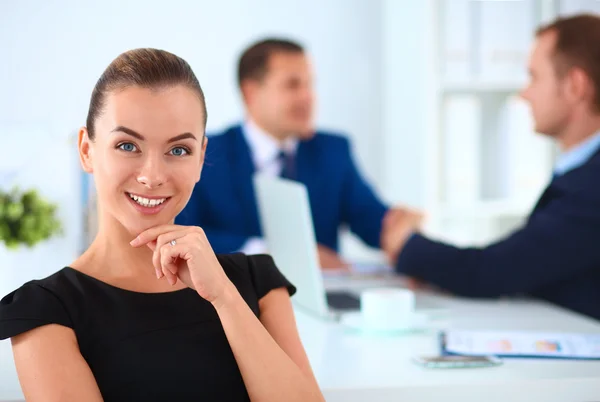 Porträt einer schönen Geschäftsfrau, die in einem Büro sitzt und Kollegen im Hintergrund die Hände schütteln — Stockfoto