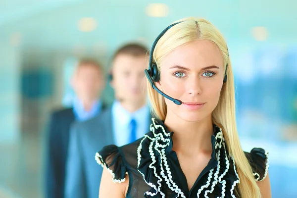 Retrato de mujer de negocios hermosa en auriculares sonriendo con colegas de fondo —  Fotos de Stock