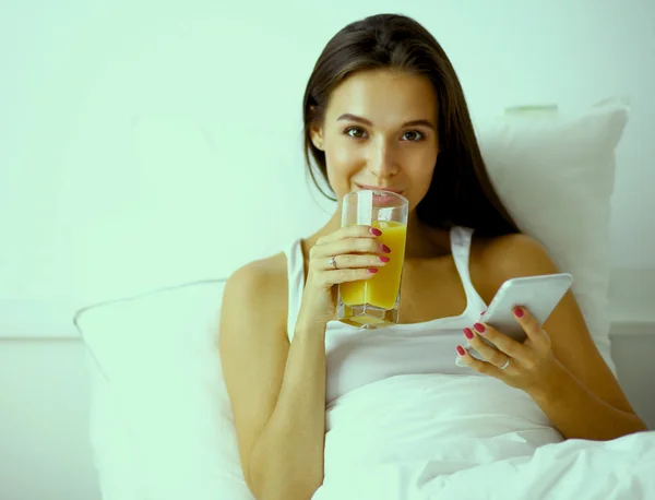 Una hermosa mujer bebiendo jugo en la cama — Foto de Stock