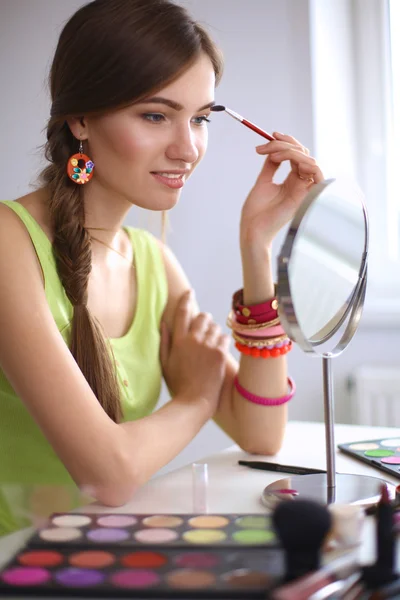 Joven hermosa mujer haciendo maquillaje cerca del espejo, sentado en el escritorio —  Fotos de Stock