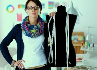 Gülümseyen moda tasarımcısı ofiste mankenin yanında duruyor.