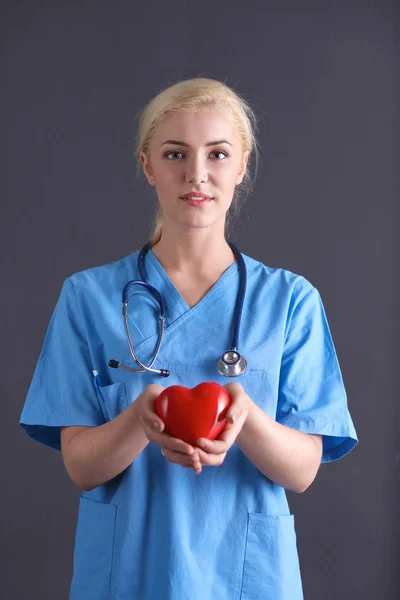 Doctor with stethoscope holding heart, isolated on gray background — Stock Photo, Image