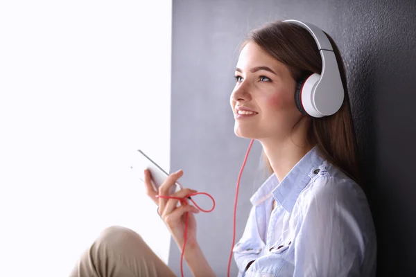 Gadis tersenyum dengan headphone duduk di lantai dekat dinding — Stok Foto
