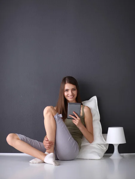 Mulher morena bonita sentada no chão com uma almofada e mesa plana — Fotografia de Stock