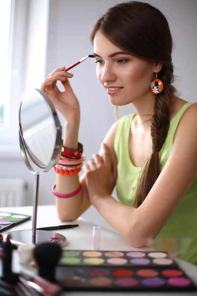 Joven hermosa mujer haciendo maquillaje cerca del espejo, sentado en el escritorio —  Fotos de Stock