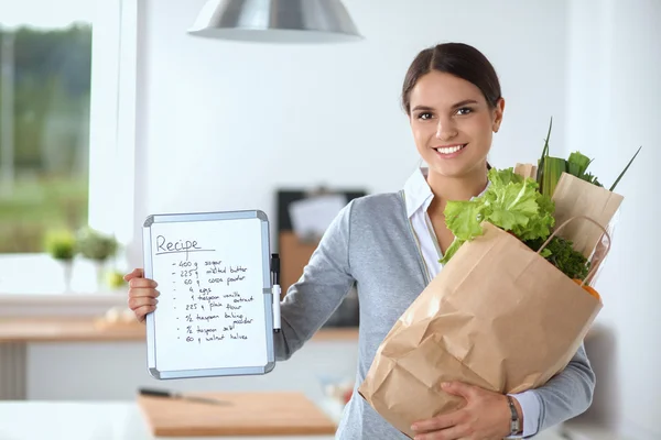 Kvinna i köket hemma, stående nära skrivbord med mapp — Stockfoto