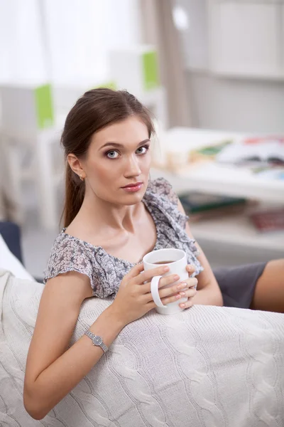 自宅でソファの上のカップを持つ若い美しい女性 — ストック写真