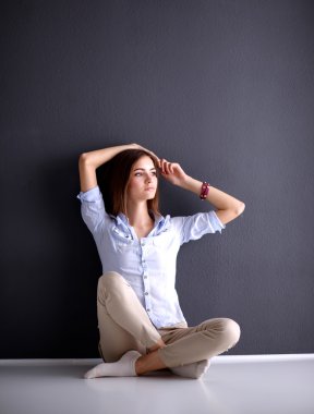 Genç bir kadın yerde, kara duvarın yanında oturuyor.