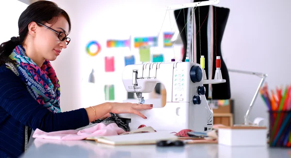 Junge Frau näht, während sie am Arbeitsplatz sitzt — Stockfoto