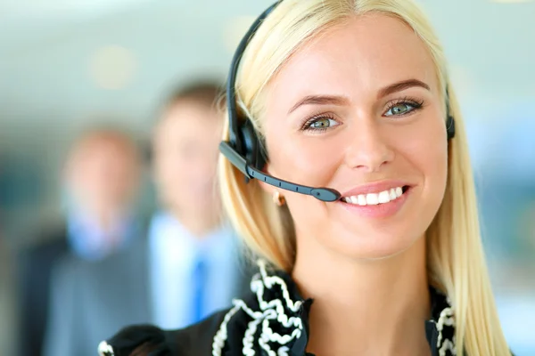 Retrato de mujer de negocios hermosa en auriculares sonriendo con colegas de fondo — Foto de Stock