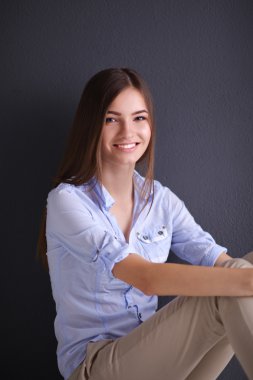 Genç bir kadın yerde, kara duvarın yanında oturuyor.