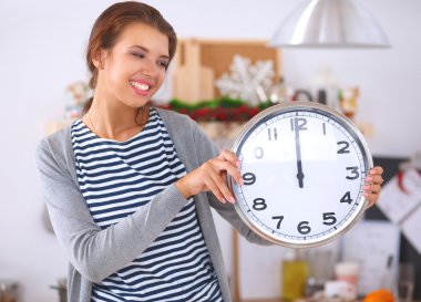 Mutlu genç kadın Noel süslemeli mutfakta saat gösteriyor.