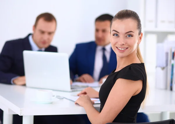 Retrato de una hermosa mujer de negocios sentada en una oficina con colegas en el fondo — Foto de Stock