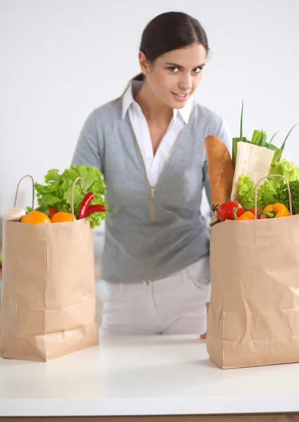 Mujer joven sosteniendo bolsa de la compra de comestibles con verduras de pie en la cocina —  Fotos de Stock