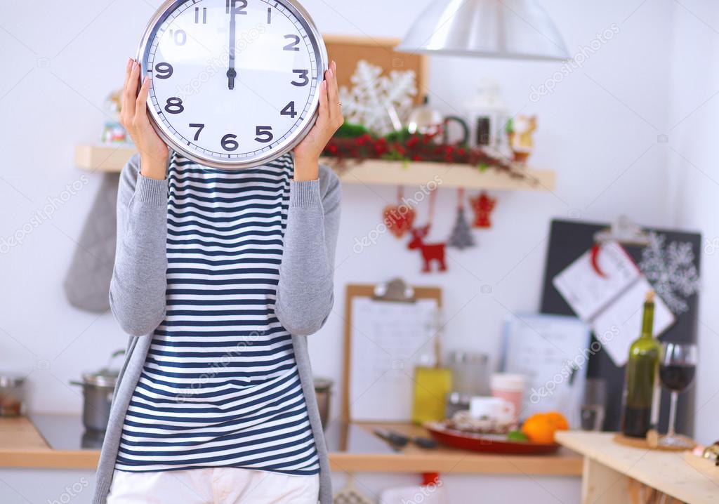 Happy young woman showing clock in christmas decorated kitchen