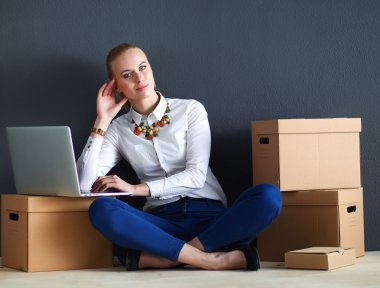 Kadın yerde dizüstü bilgisayarlı bir kutunun yanında oturuyor.