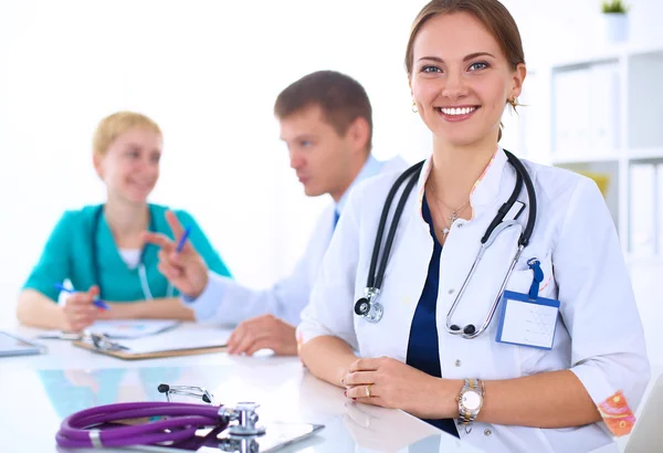 Bonito jovem sorridente médico feminino sentado na mesa — Fotografia de Stock