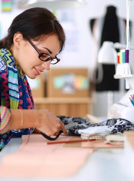 Fashion designer cutting textile next to a sewing machine — Stock Photo, Image