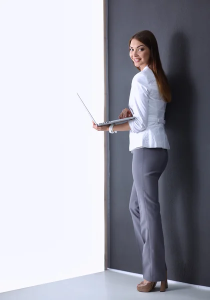 Jonge vrouw met een laptop, staande op een grijze achtergrond — Stockfoto
