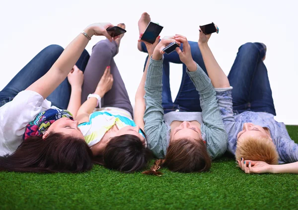 Чотири молодих жінки лежать на зеленій траві з мобільним телефоном — стокове фото