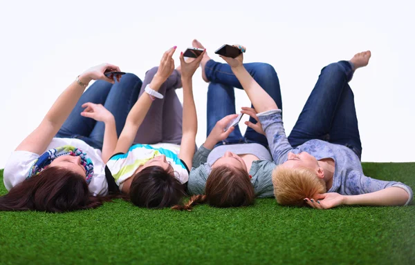 Four young women lying on green grass with mobile phone — Stock Photo, Image