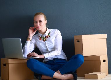 Kadın yerde dizüstü bilgisayarlı bir kutunun yanında oturuyor.