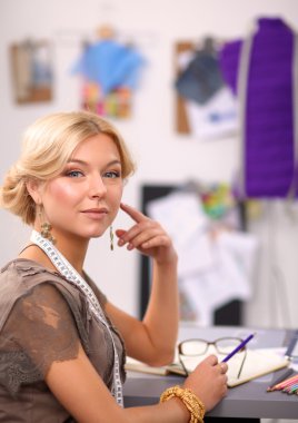 Gülümseyen kadın moda tasarımcısı ofis masasında oturuyor.