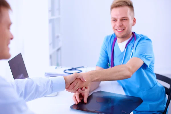 医生和病人握手，坐在办公室的桌子上 — 图库照片