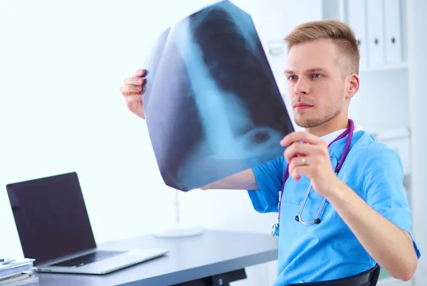 Retrato de um médico masculino sorridente com laptop sentado na mesa no consultório médico — Fotografia de Stock