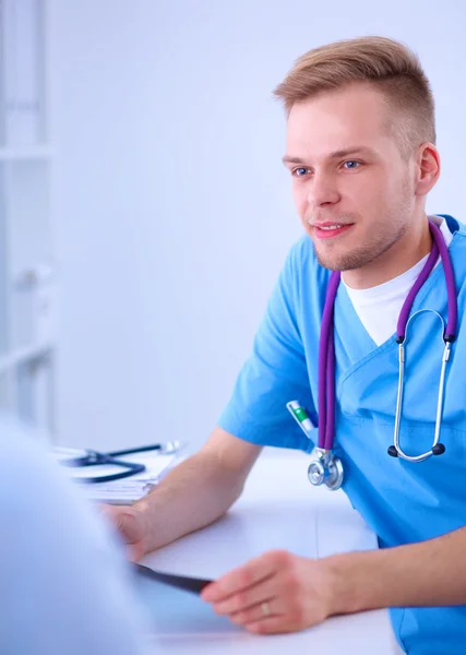 Retrato de un médico varón sonriente con portátil sentado en el escritorio en el consultorio médico — Foto de Stock