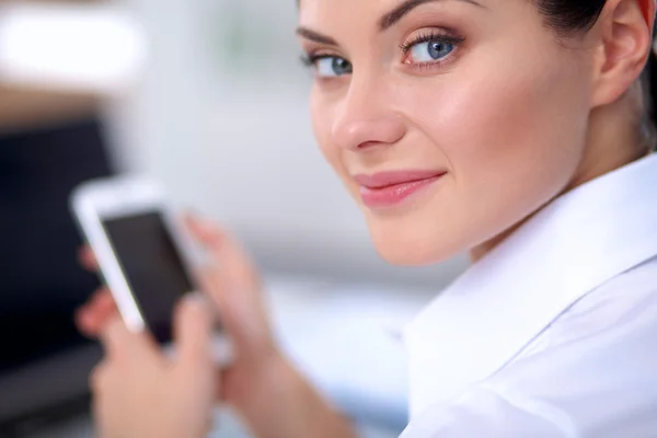 Businesswoman sending message with smartphone sitting in the office — Stock Photo, Image