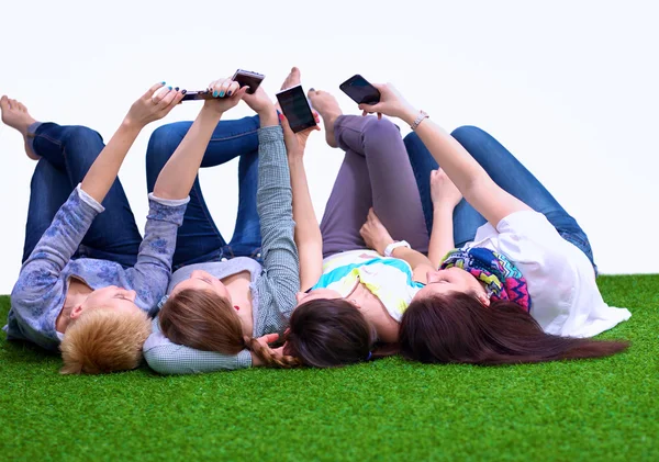 Cuatro mujeres jóvenes tumbadas en hierba verde con teléfono móvil — Foto de Stock